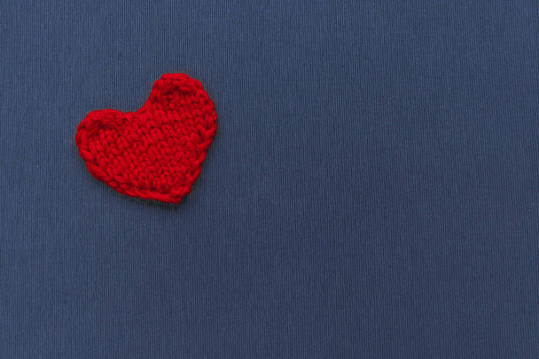 Red heart knitted from threads on a blue background - Foto, afbeelding