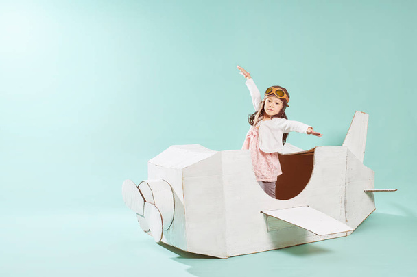 Little cute girl playing with a cardboard airplane. White retro style cardboard airplane on mint green background . Childhood dream imagination concept . - Photo, Image