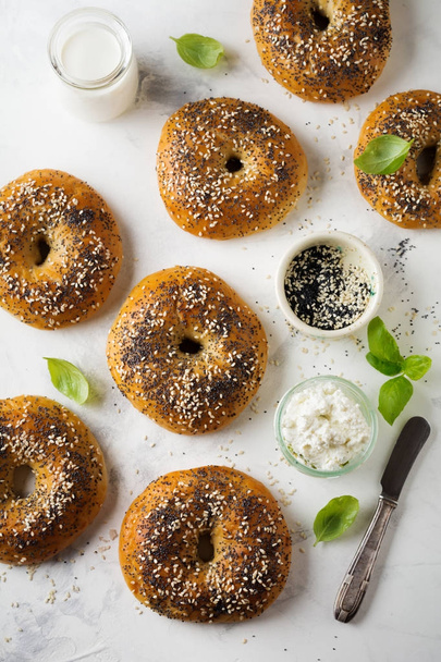 Variety fresh whole-grain bagels with poppy seeds, sesame seeds and ingredients for breakfast  on  light concrete  background. - Valokuva, kuva