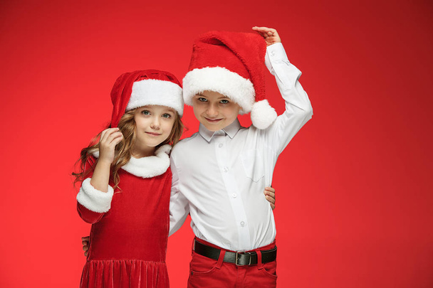 Two happy boy and girl in santa claus hats with gift boxes at studio - Фото, изображение