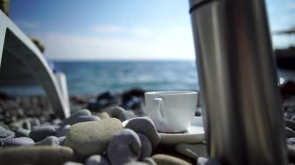 A cup of coffee with blue sea. White Cup on the rocks on the shore - Footage, Video