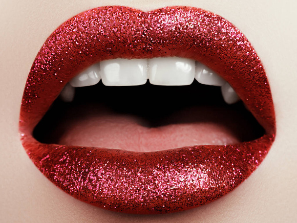 キラキラとグラマラス ファッション真っ赤な唇をメイク。女性の顔の部分のマクロ。高級女性のセクシーな光沢のある唇のメイクアップ - 写真・画像