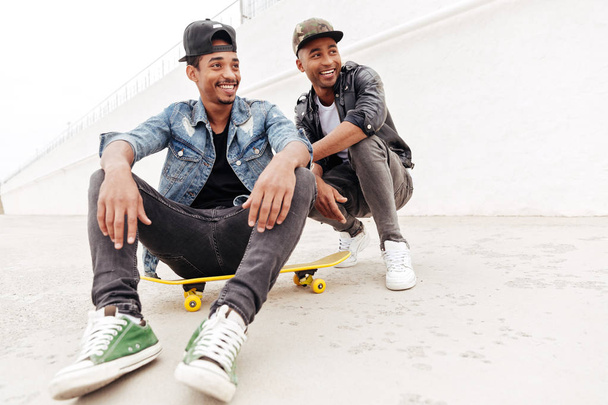 African men friends walking outdoors sitting with skateboard - Valokuva, kuva