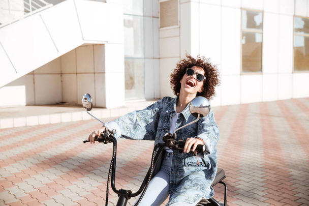 Side view of laughing girl in sunglasses posing on motorbike - Photo, Image