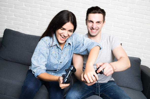Νεαρό ζευγάρι παίζοντας βιντεοπαιχνίδια με διασκέδαση στο σπίτι - Φωτογραφία, εικόνα