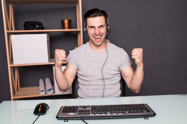 молодой счастливый человек с гарнитурой играет и выигрывает компьютерную игру дома
 - Фото, изображение