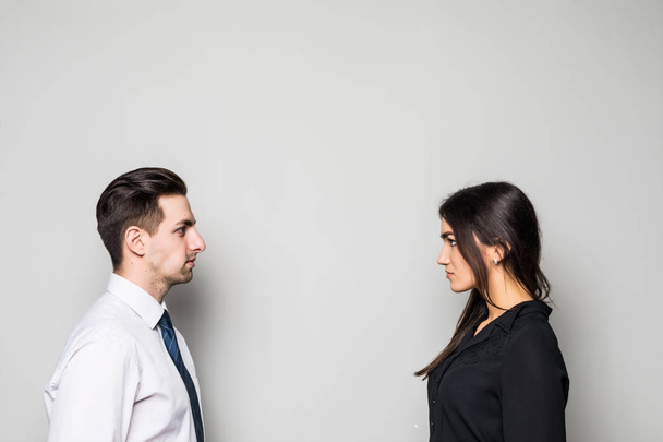 Concept of confrontation in business. Close up photo of two young serious confident people standing face-to-face to each other on gray - Photo, Image