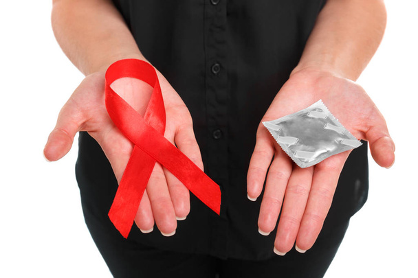 Close-up picture of a red ribbon and a packed condom on female hands isolated on a white background. Solidarity of people living with AIDS. Healthy lifestyle concept. Copy space. - Valokuva, kuva