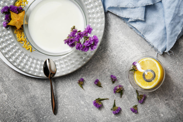 A view from above of a composition of summer dessert. A glass of white, organic milk smoothie or yogurt with blue fabric, purple flowers and exotic carambola on a light gray background.  - Foto, imagen