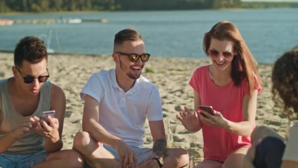 Mladí lidé, které baví na pláži pomocí telefonů - Záběry, video
