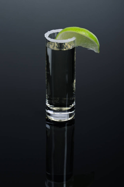 Alcoholic cocktail in shot glass. Hot mexican tequila served in a glass with salt on dark gray background. - Foto, imagen
