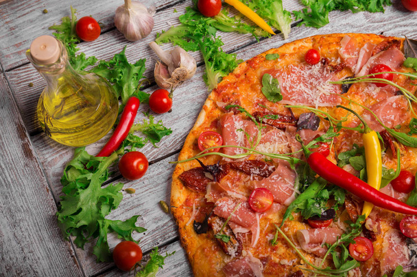 Вид сверху на вкусную пиццу пепперони с овощами, бутылку оливкового масла и листья салата. Вкусное яркое блюдо на деревенском деревянном фоне. Итальянская кухня. Концепция приготовления пищи
. - Фото, изображение