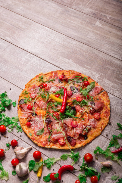 A close-up picture of a tasty vegetable pizza with cherry tomatoes and salad leaves. Delicious bright dish on a rustic wooden table background. Italian cuisine. Cooking concept. Copy space. - Photo, Image