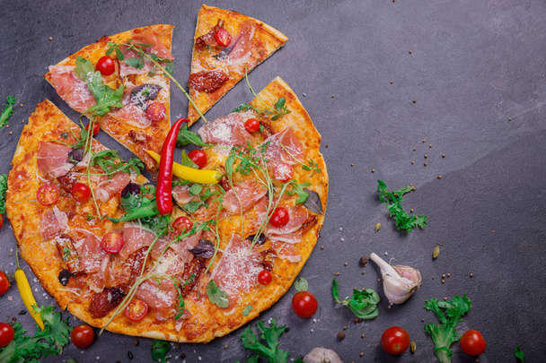 Close-up of appetizing mediterranean pizza with meat, red hot chili pepper, and basil on a dark stone background.  - Foto, Imagem