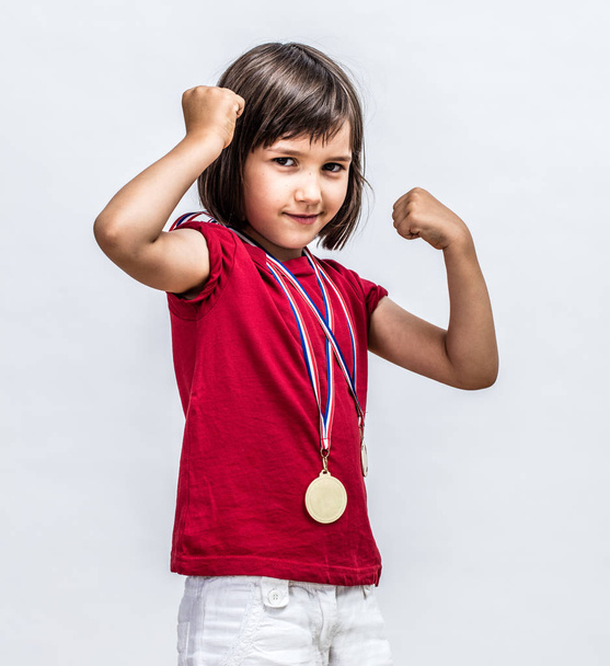 Little cheeky girl with medals smiling, showing young female power - Фото, изображение