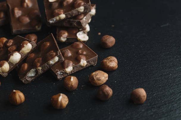 Chocolate bar pieces and nuts on dark slate background with copy space. Chocolate background. Top view. Toned - Foto, imagen