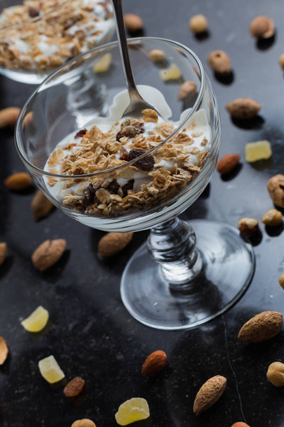 Muesli met yoghurt, noten en vruchten in glazen kom op donkere achtergrond. Heerlijke, gezonde zoete dessert voor het ontbijt. Granen, muesli. Kopie ruimte, close-up - Foto, afbeelding