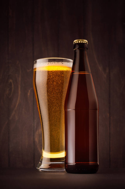 Brown beer bottle NRW and glass weizen with golden lager on dark  wood board, vertical, mock up.  - Фото, изображение
