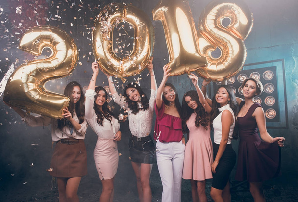 Šťastný rok 2018! Ruce nahoru! Zábava je vše, co potřebujeme! Krásná skupina usmívající se dívky, nesoucí zlato barevné čísla 2018 režii a hází konfety - Fotografie, Obrázek
