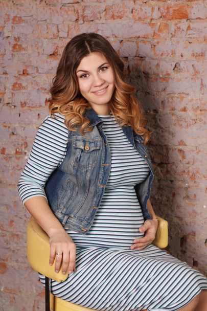 beautiful pregnant woman in striped dress, jacket is sitting - Foto, Bild