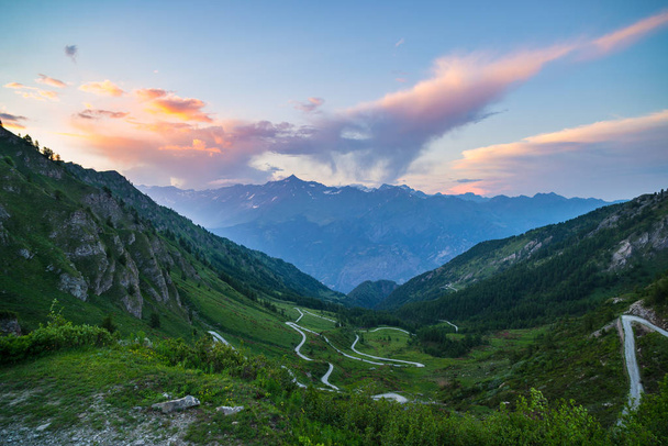 Mountain road leading to high mountain pass on the Italian Alps.. Expasive view at sunset, colorful dramatic sky, adventure road trip in summer. - Photo, Image