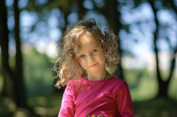 Милая маленькая девочка, весёлый вид, вьющиеся волосы, милая улыбка, солнечный летний портрет
 - Фото, изображение