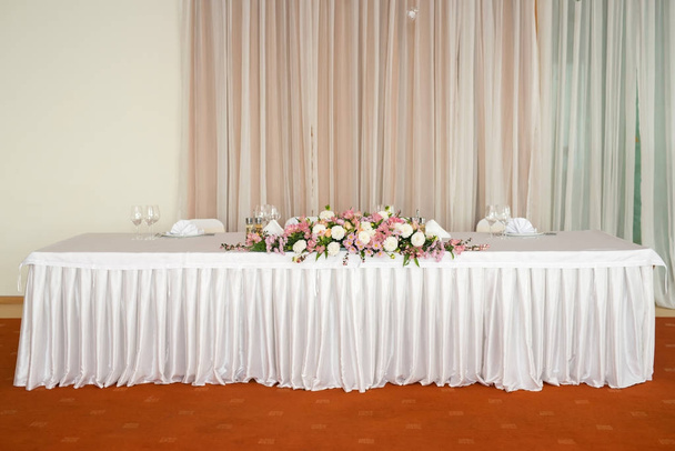 Beautiful wedding floral decoration on a table in a restaurant.White tablecloths, bright room. - Photo, Image