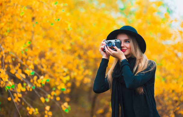 young woman photographing outdoors in autumn. Yellow leaves background - Fotó, kép