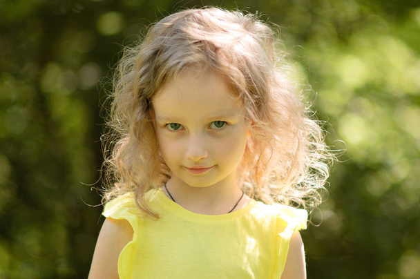 Detailní portrét skeptický holčička se dívá podezíravě, skeptický, úsměvu, ironicky. Portrét v pozadí zelené dřevo - Fotografie, Obrázek
