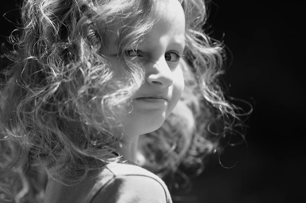 Portrait extérieur d'une jolie petite fille aux oreilles bouclées, regardant par-dessus son épaule. noir et blanc
 - Photo, image