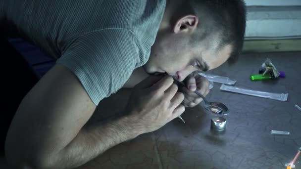 Ένας τύπος που είναι εθισμένος στα ναρκωτικά κάθεται στο πάτωμα και ετοιμάζει μια δόση σε ένα κουτάλι πάνω από ένα κερί. - Πλάνα, βίντεο