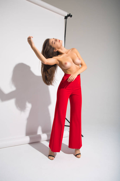 schöne nackte Frau in roten Hosen posiert Schatten werfen isoliert auf dem grauen Hintergrund - Foto, Bild