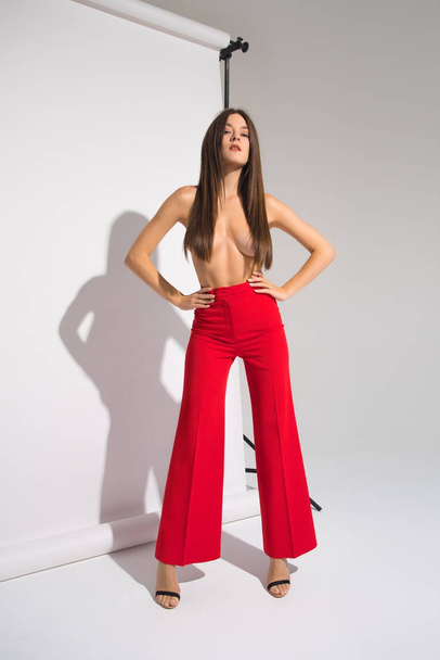 Kaunis alaston nainen punaisissa housuissa poseeraus valu varjo eristetty harmaalla taustalla
 - Valokuva, kuva