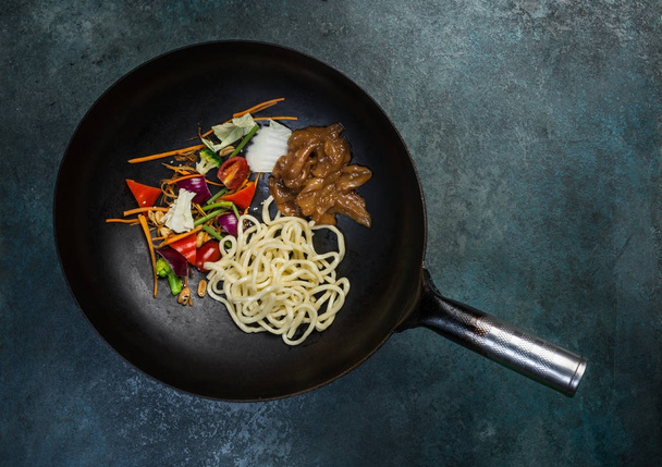 Aziatische Wok - traditionele Oosterse pan met ruwe ingrediënten op een vintage gekleurde achtergrond. Bovenaanzicht - Foto, afbeelding