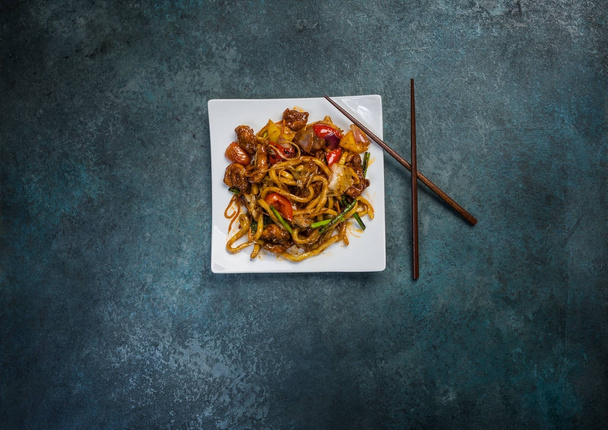 Udon roer bak noedels met vlees of eend en groenten op een vierkant wit bord. Met stokjes. Bovenaanzicht - Foto, afbeelding