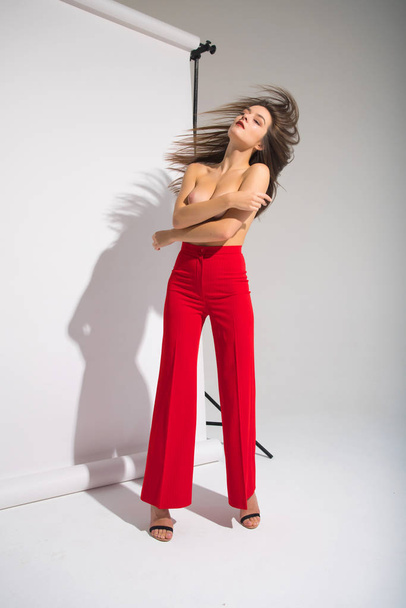 Beautiful Naked Woman In Red Pants Posing Casting Shadow Isolated On The Gray Background - 写真・画像