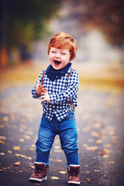happy laughing toddler baby boy with red hair having fun at autumn park - Fotó, kép