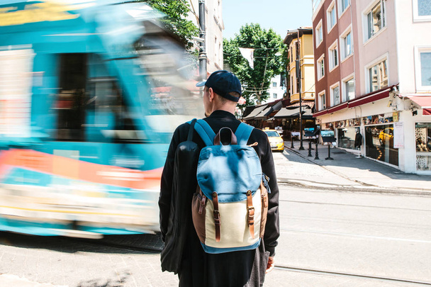 Yol tramvay ile önünde dostum. Sırt çantası ile rahat kıyafetler erkek turist önünde duruyor yol tramvay ile güneşli yaz günü geçiyor. Hareket Bulanıklığı. - Fotoğraf, Görsel