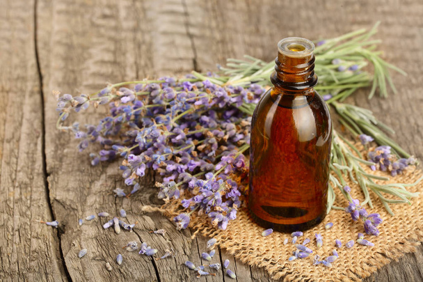 Herbal oil and lavender flowers on old wooden background - 写真・画像