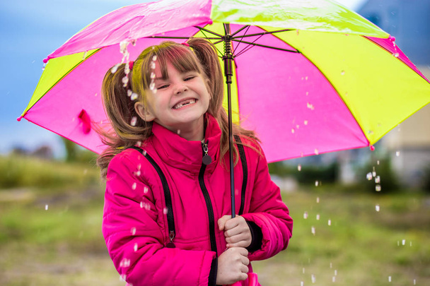 Tyttö sateenvarjon kanssa nauttii sateesta.
 - Valokuva, kuva