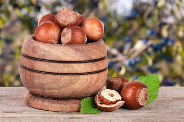 Lískové ořechy s listy v dřevěné misce na dřevěný stůl s rozmazané pozadí zahradní - Fotografie, Obrázek