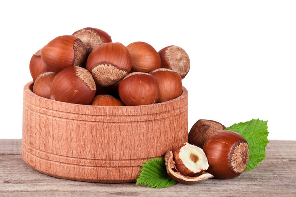 Hazelnuts with leaves in a wooden bowl on a wooden table with a white background - Photo, Image