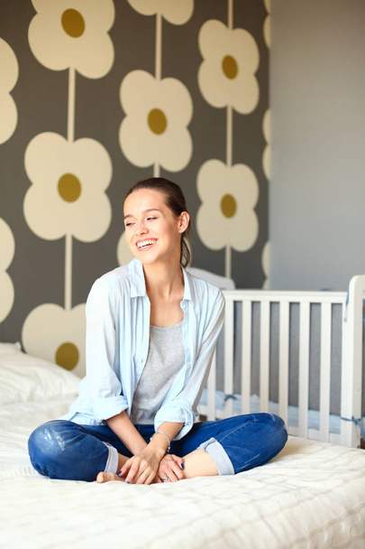 Young woman sitting on the bed near childrens cot. Young mom - Foto, imagen