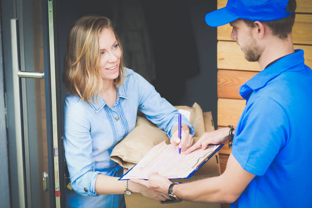 Smiling delivery man in blue uniform delivering parcel box to recipient - courier service concept. Smiling delivery man in blue uniform - Zdjęcie, obraz