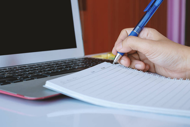 Hand holding een pen om te schrijven op de notebook en met behulp van een computer laptop voor werk, technologie en business concept - Foto, afbeelding