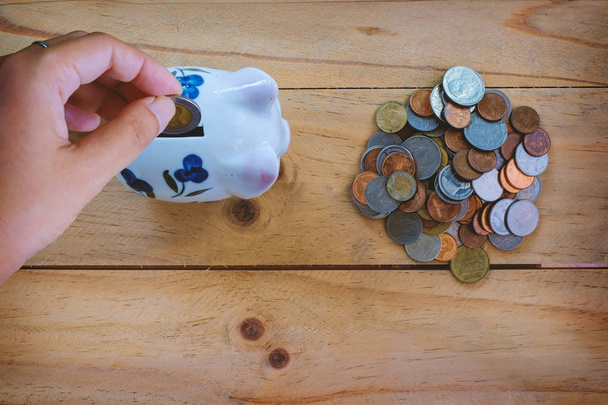 Vista superior de la moneda de ahorro de mano a la alcancía y una pila de monedas de baht tailandés en la mesa de madera para el concepto de negocios y finanzas
 - Foto, imagen