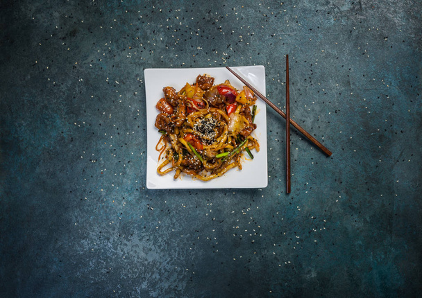 Udon stir fry noodles with meat or duck, vegetables and sesame seeds on a square white plate. With chopsticks. - Photo, Image