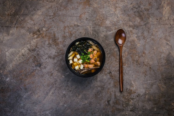 Japoński miso zupa z tofu i łososia w misce czarny na vintage kolorowym tle drewnianą łyżką. Widok z góry - Zdjęcie, obraz