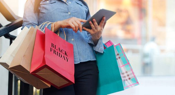 Frau benutzt Tablet und hält Black-Friday-Einkaufstüten in der Hand - Foto, Bild