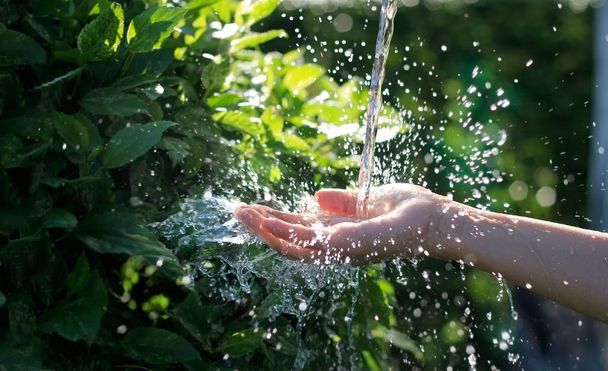 Wasser ergießt sich in Frauenhand auf Naturhintergrund, Umweltthema - Foto, Bild